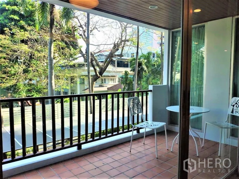 Condominium for rent in Bang Rak, Bangkok - Covered balcony with terracotta tiles, railing, and bistro chairs overlooking greenery.