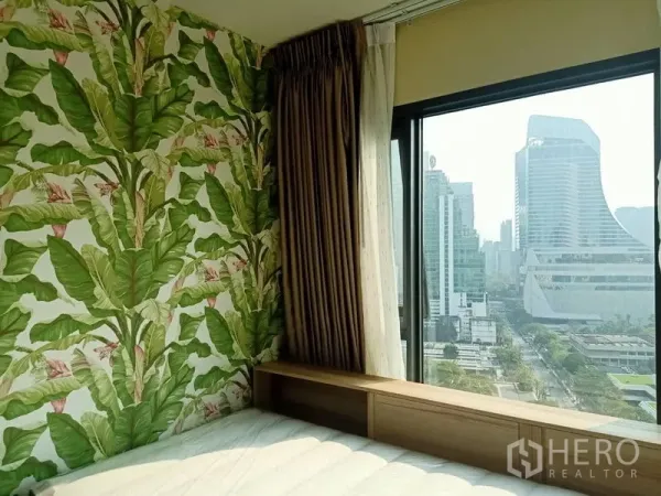 Condominium for rent in Pathum Wan, Bangkok - Bedroom corner with tropical leaf feature wall and a large window overlooking the Bangkok skyline.