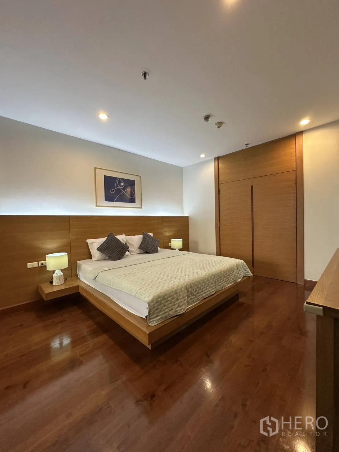 Condominium for rent in Watthana, Bangkok - Master bedroom with wood floors, king bed, and warm lighting.