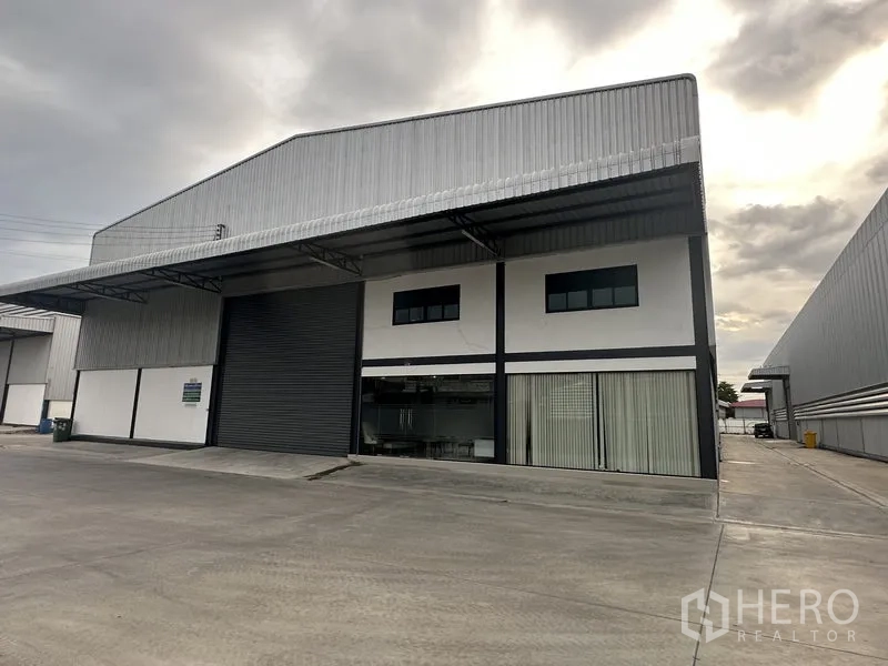 คลังสินค้า ให้เช่าในBang Phli, Samut Prakan - มุมมองด้านหน้าโกดังผนังเมทัลชีท ประตูม้วนขนาดใหญ่ สำนักงานกระจก และลานคอนกรีตกว้าง