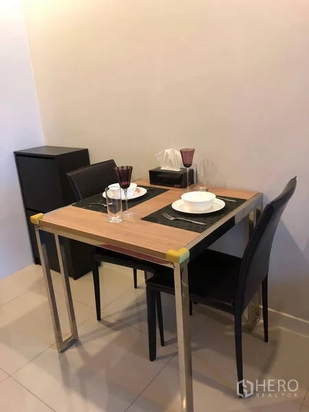 Condominium for sale in Ratchathewi, Bangkok - Compact dining nook for two with a wooden table, place settings and a mini fridge.