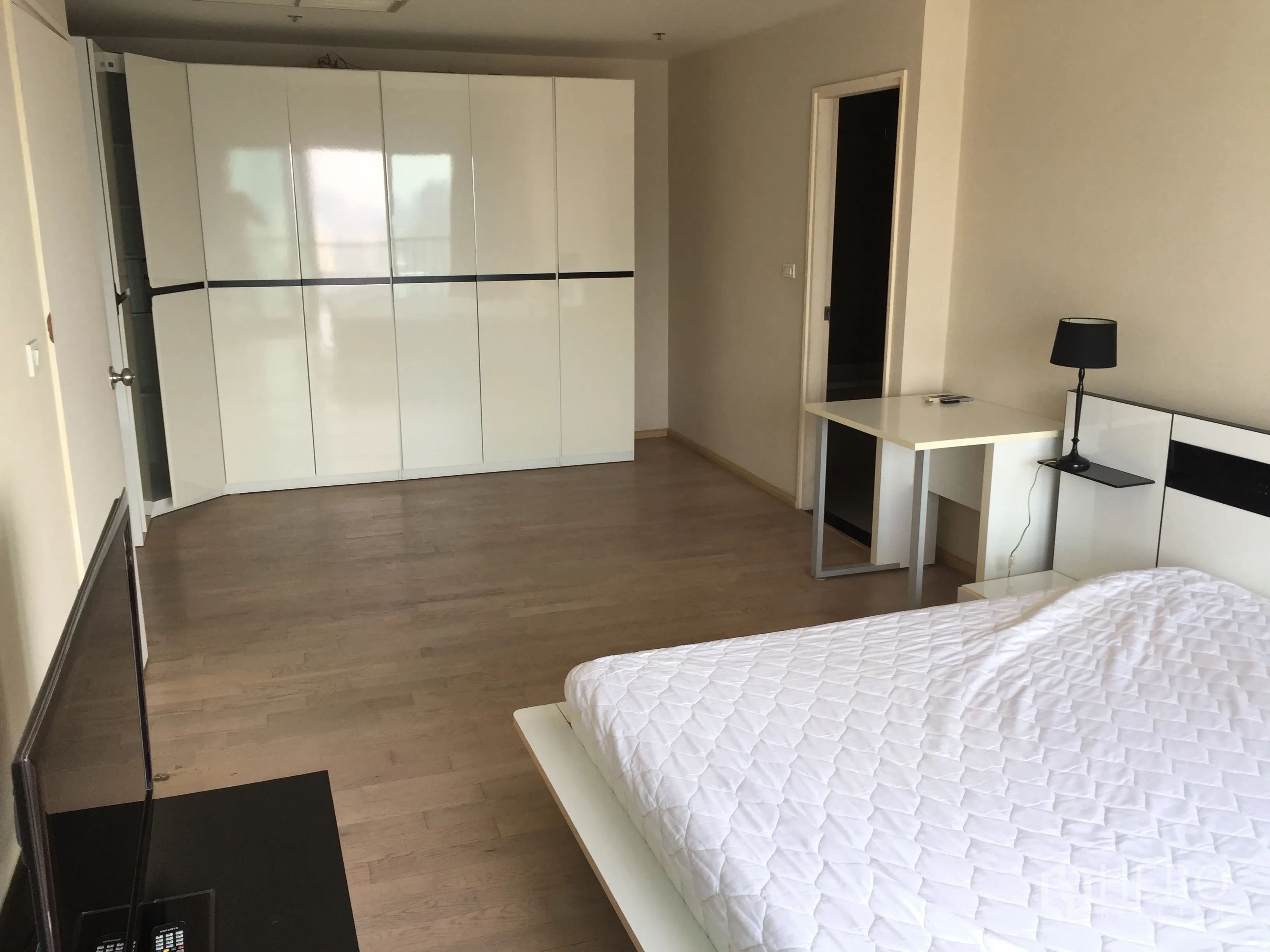 Condominium for rent in Khlong Toei, Bangkok - Spacious master bedroom with glossy white wardrobes and a study desk.