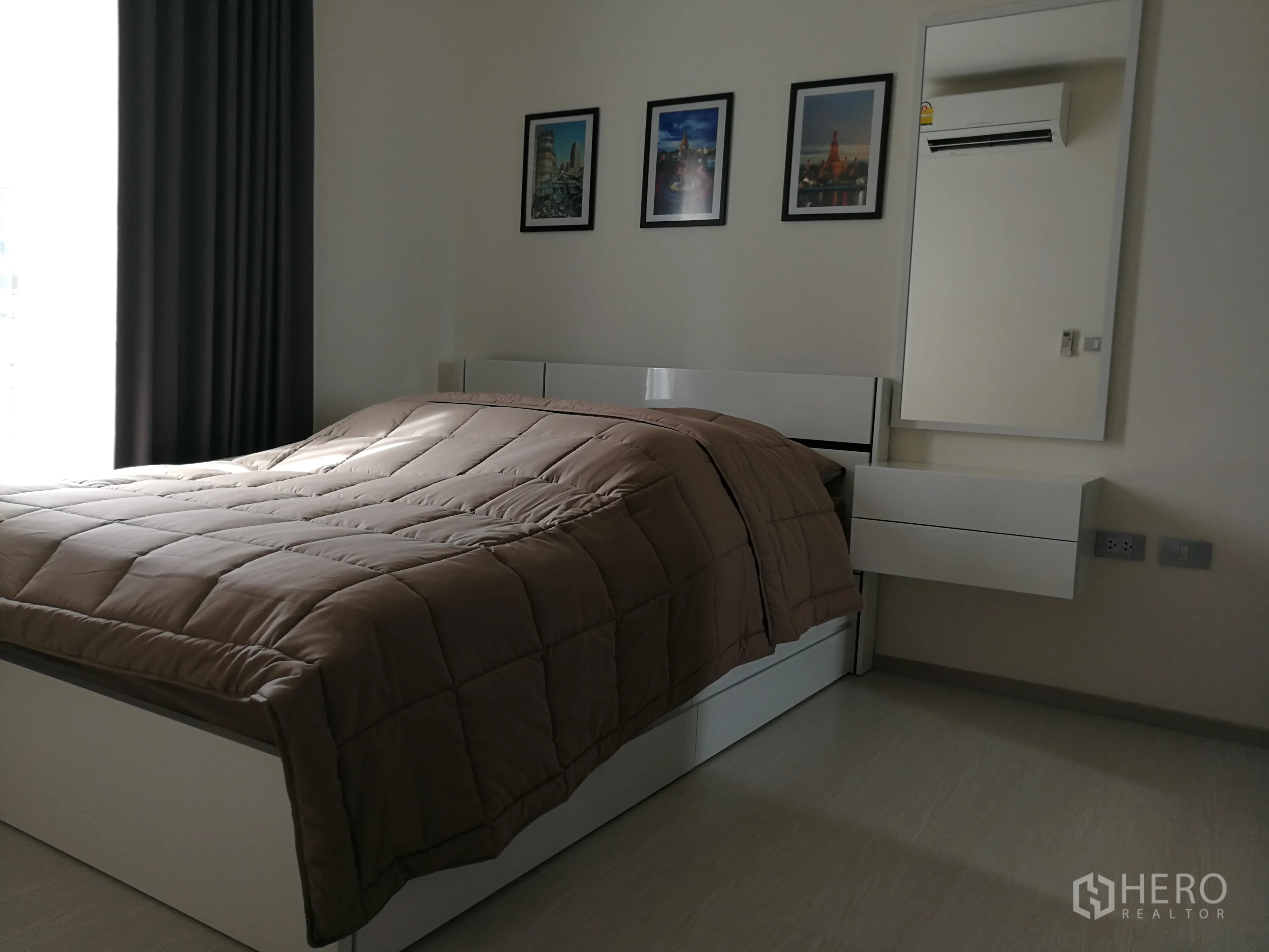 公寓 出租在Khlong Toei, Bangkok - 温馨卧室，双人床、深色窗帘、墙面装饰画与带镜梳妆台。