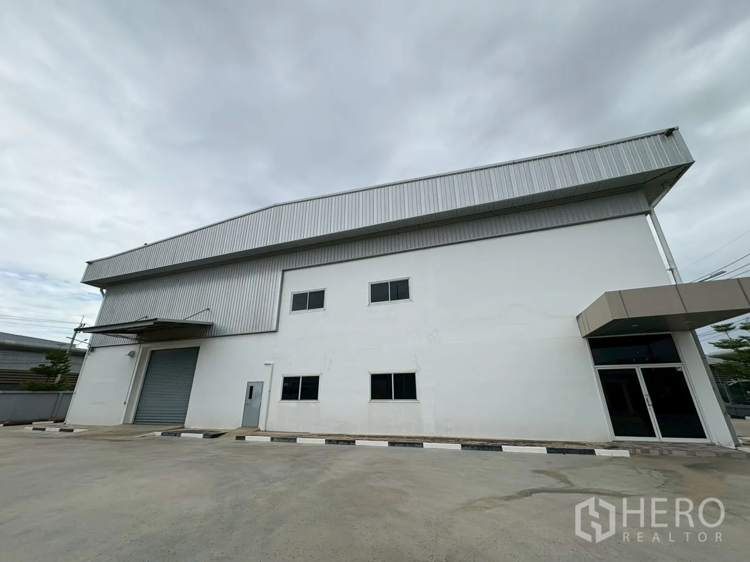 Factory for sale in Bang Bo, Samut Prakan - Modern white factory exterior with high gable roof and roller shutter gate.