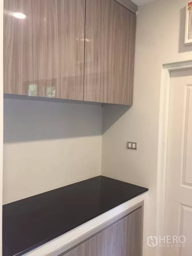 Detached House for rent in Samut Prakan - Storage counter with upper cabinets and a black worktop beside an interior door.