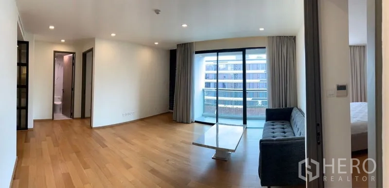 Condominium for sale in Khlong Toei, Bangkok - Bright living room with wood floors, sofa, coffee table and sliding doors opening to a balcony with city views.