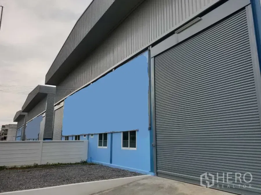 工厂 出售在Sai Noi, Nonthaburi - 暖武里Sai Noi现代钢结构工厂外观，蓝色立面与大型卷闸门。