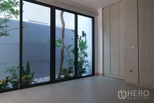 联排别墅 出租在Watthana, Bangkok - 一层房间，落地玻璃面向口袋花园，浅木色衣柜。