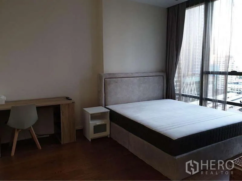 Condominium for rent in Sathon, Bangkok - Bright bedroom with large window, upholstered bed and work desk facing the city.
