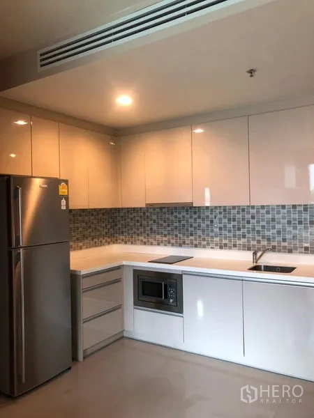 公寓 出售在Bang Rak, Bangkok - L形厨房，亮面橱柜、马赛克墙面与内置家电。