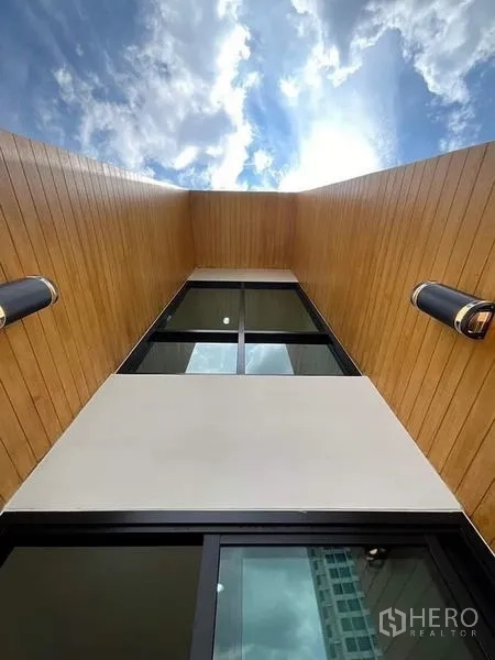 Townhouse for sale in Watthana, Bangkok - Upward view of vertical wood cladding framing a tall window against the sky.