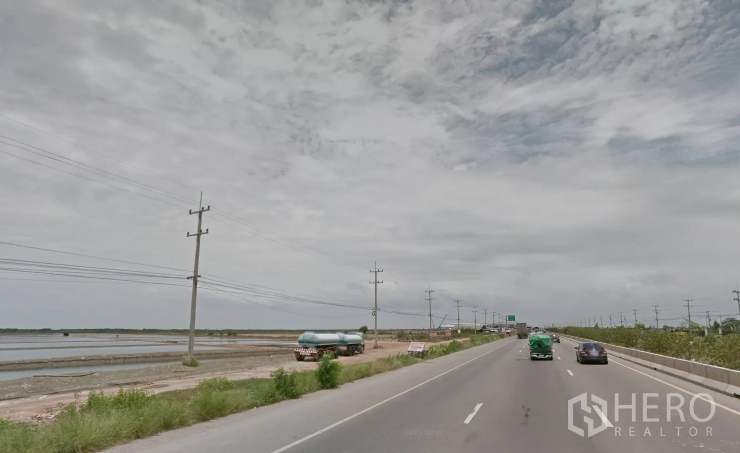 Land for sale in Mueang Samut Sakhon, Samut Sakhon - View along the highway showing utility poles, vehicles, and broad open land beside the road.