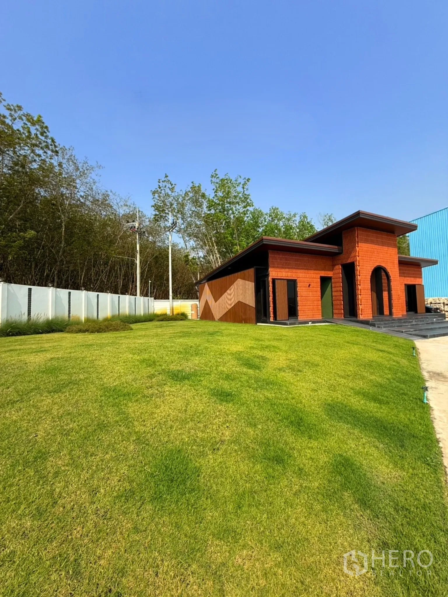 Factory for sale in Ban Bueng, Chon Buri - Modern low-rise office pavilion with orange brick facade set by a grassy lawn and trees.
