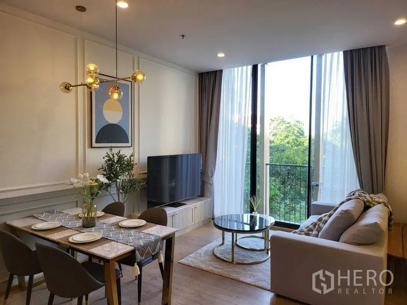 Condominium for rent in Watthana, Bangkok - Open living and dining space with chandelier, TV and balcony doors framing greenery outside.