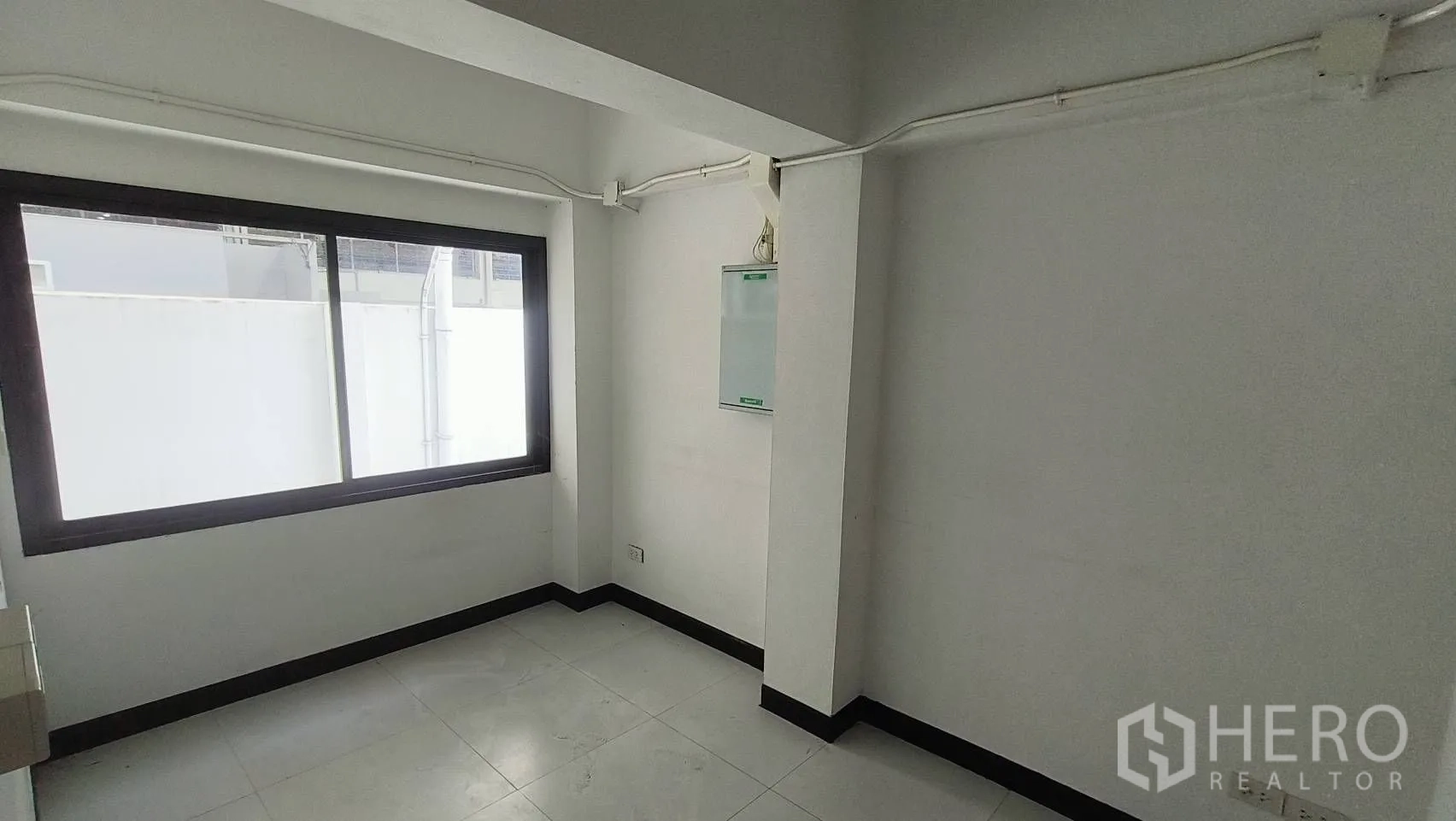 Office Space for rent in Khlong Toei, Bangkok - Small room with window, exposed conduit and electrical panel.