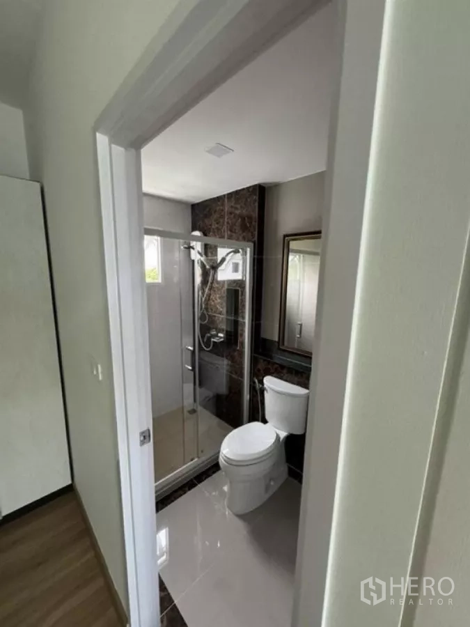 Detached House for rent in Thanyaburi, Pathum Thani - Modern bathroom with glass shower enclosure, toilet and tiled walls.