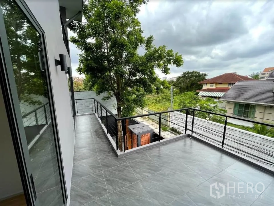 Detached House for sale in Watthana, Bangkok - Spacious tiled balcony with metal railing and green neighborhood views.