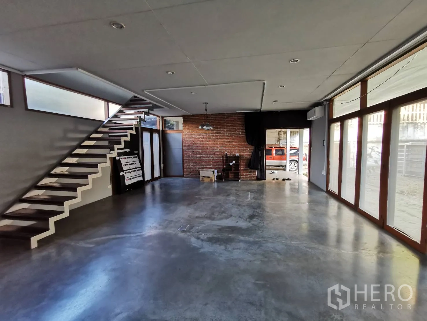 Home Office for rent in Watthana, Bangkok - Open-plan ground floor with floating staircase, concrete floor and brick accent wall.