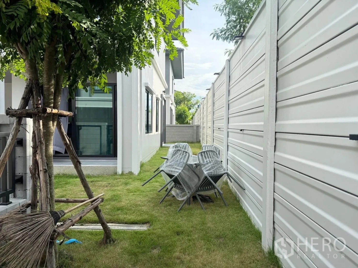 Detached House for rent in Bang Phli, Samut Prakan - Private lawn with a tree, stacked outdoor chairs and a sliding glass door.