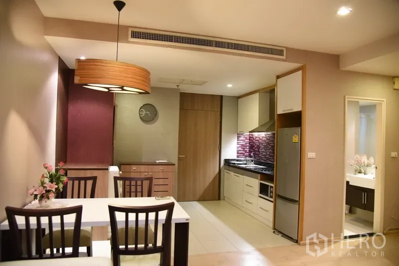 Condominium for rent in Khlong Toei, Bangkok - Compact kitchen with stainless fridge, cooktop, hood and mosaic backsplash beside the dining space and bathroom entrance.