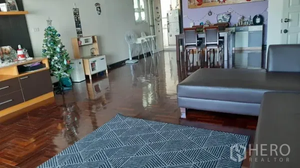 Condominium for rent in Watthana, Bangkok - Open-plan living and dining room with polished hardwood floors, brown sectional sofa, and a dining set beside the kitchenette.