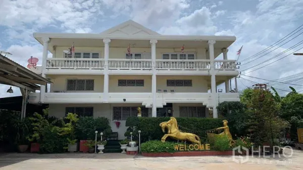 Warehouse for rent in Phra Pradaeng, Samut Prakan - Three-storey office building with balconies facing a concrete yard and garden statues.