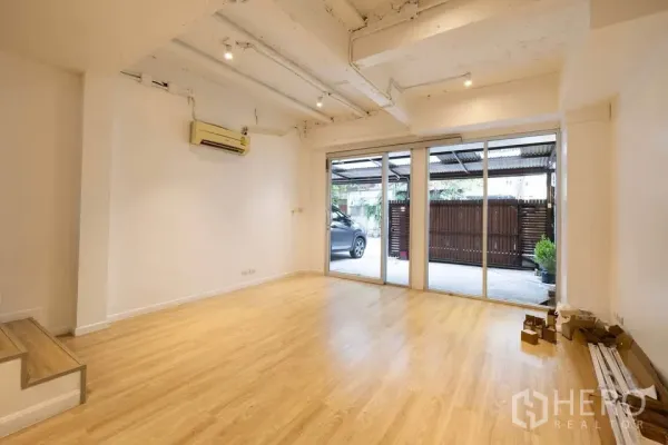 联排别墅 出租在Khlong Toei, Bangkok - 一楼客厅采光充足，木地板，超宽推拉玻璃门通向车棚。