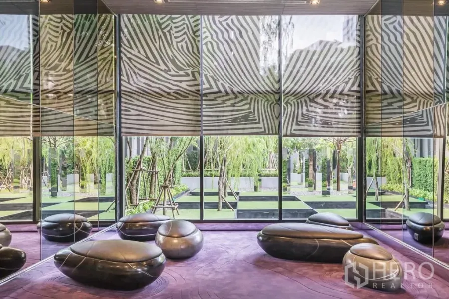 Condominium for rent in Khlong Toei, Bangkok - Modern condo lounge with mirrored walls, sculptural seating and garden views.