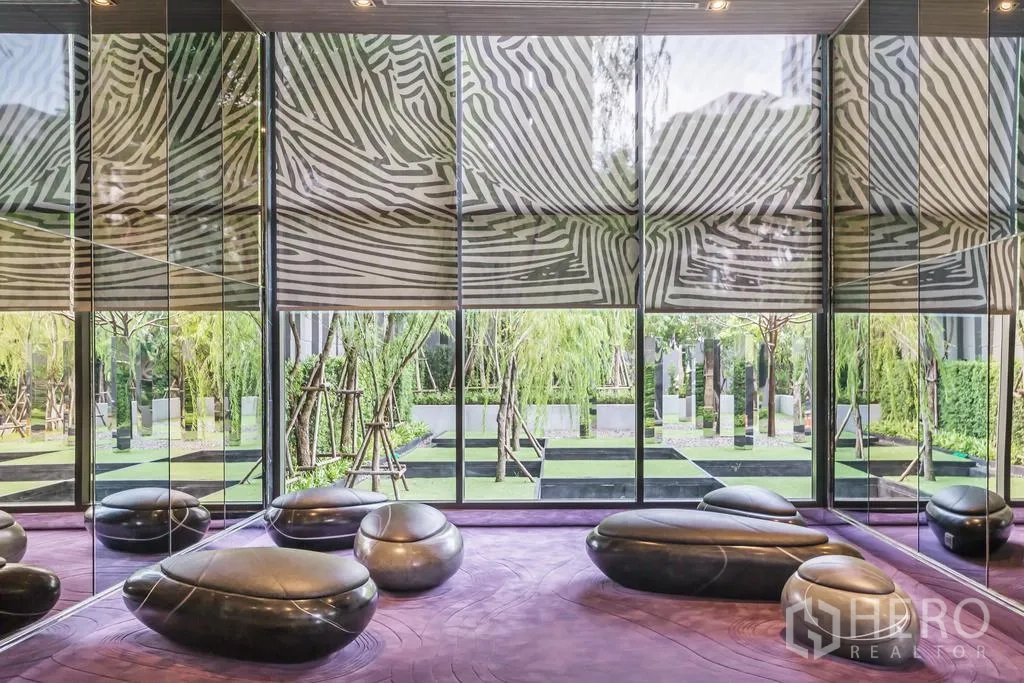 Condominium for rent in Khlong Toei, Bangkok - Modern condo lounge with mirrored walls, sculptural seating and garden views.