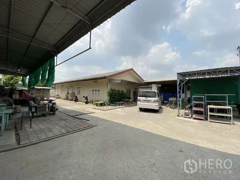 Factory for sale in Khlong Luang, Pathum Thani - On-site staff accommodation and workshop sheds with open parking inside the factory compound.