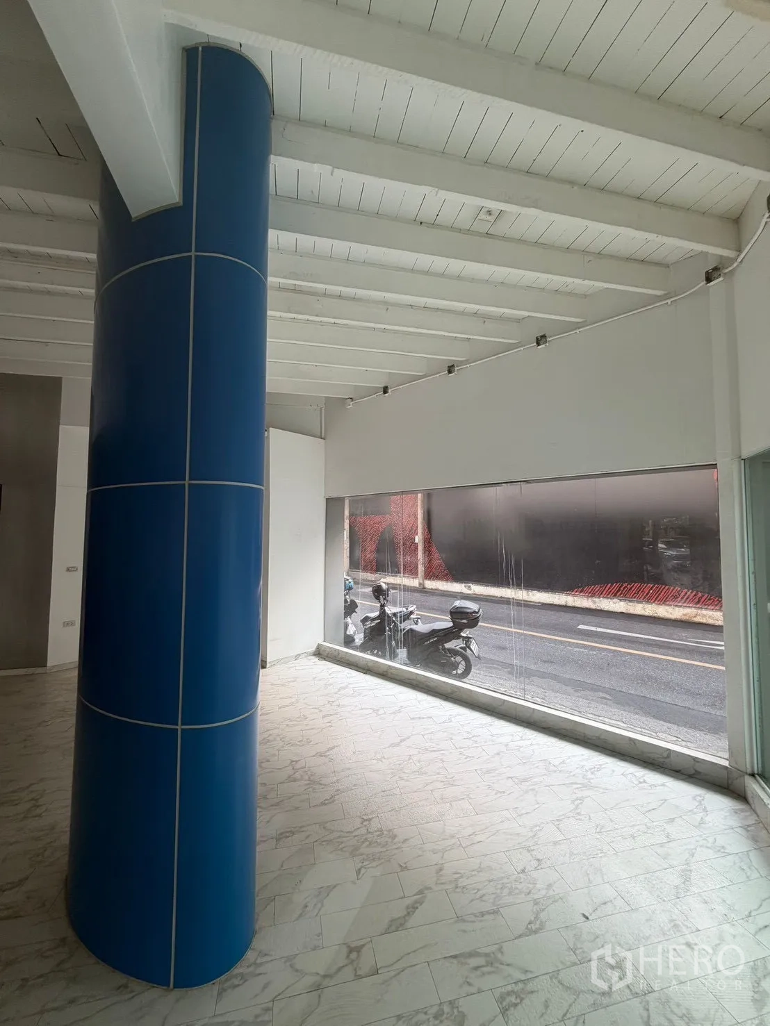 Shophouse for rent in Watthana, Bangkok - Interior view with a blue column, white ceiling beams, and a floor-to-ceiling window.
