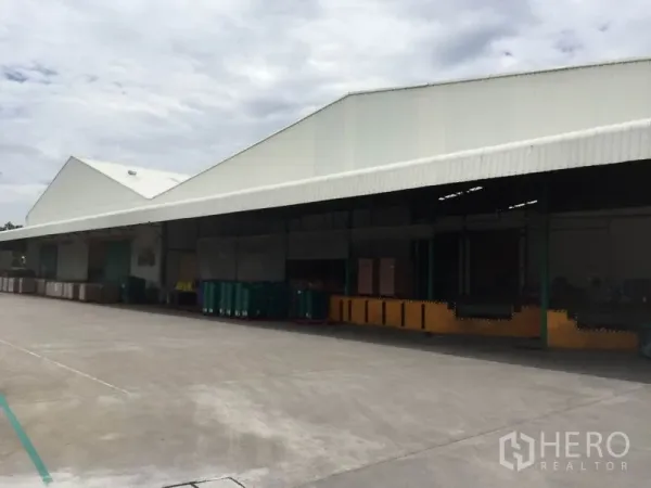 Warehouse for rent in Pak Kret, Nonthaburi - Long white warehouse exterior with wide covered loading bays and a large concrete yard.