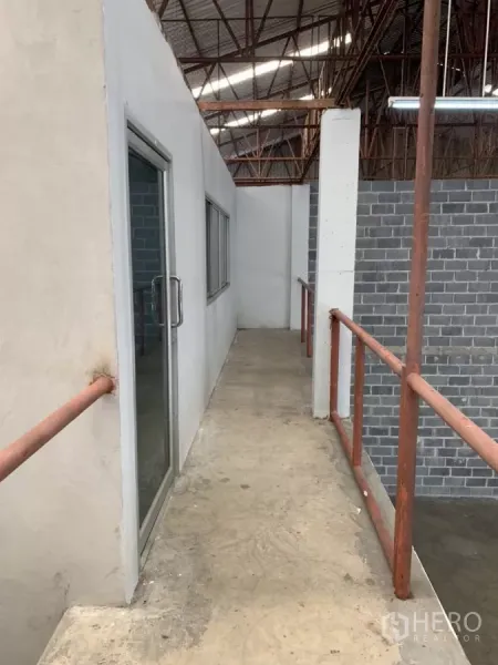 Warehouse for rent in Min Buri, Bangkok - Upper-level walkway with metal railings leading to glass office doors inside the warehouse.