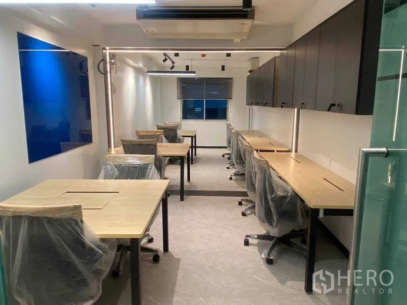 Office Space for rent in Khlong Toei, Bangkok - Modern 45 sqm office with long wooden desks, rolling chairs, overhead cabinets, track lighting and a glass entry door.