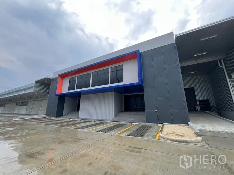 Warehouse for rent in Chon Buri - Modern warehouse exterior with bold facade, covered loading and marked parking bays in Phan Thong, Chon Buri.
