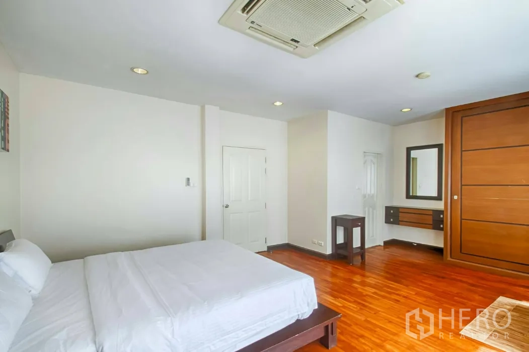 Townhouse for rent in Watthana, Bangkok - Large bedroom with wood floors, built-in wardrobe and ensuite access.