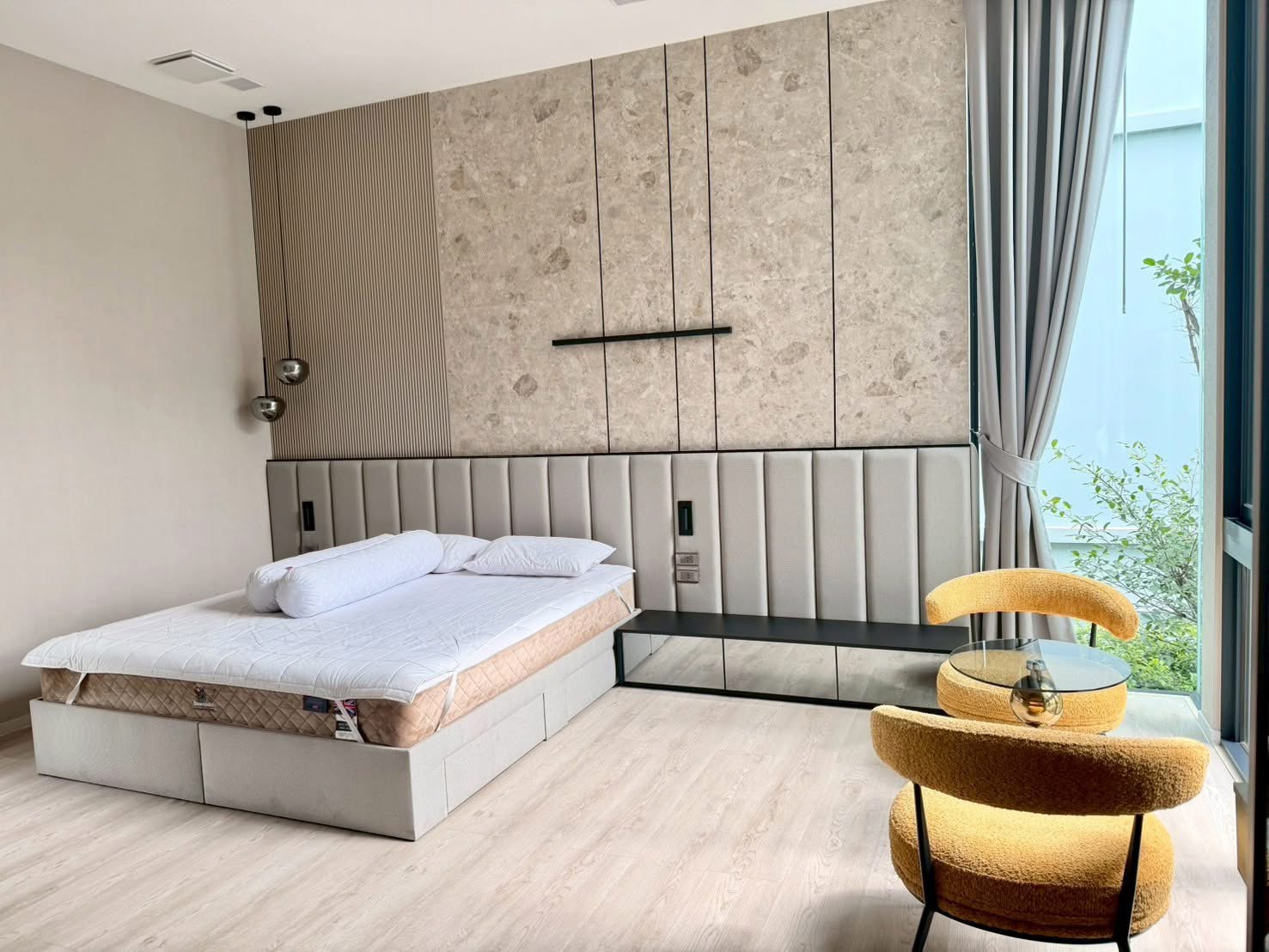 Detached House for rent in Saphan Sung, Bangkok - Modern bedroom with textured headboard wall, pendant lights and a corner lounge chair by the window.
