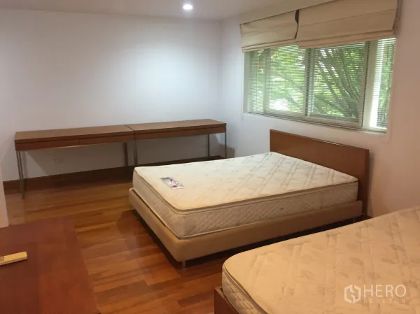 Detached House for rent in Watthana, Bangkok - Spacious bedroom with twin beds, long built-in desk and green garden views.