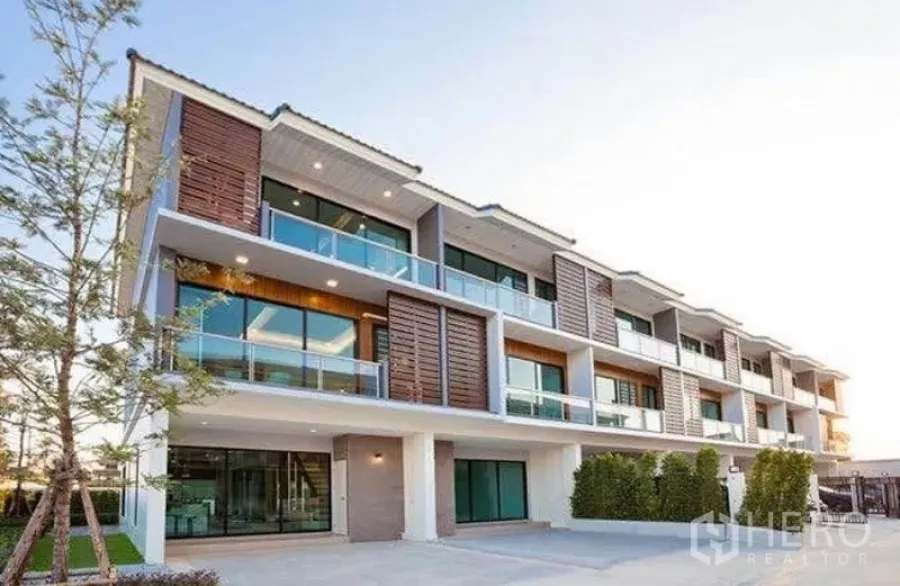 Townhouse for rent in Bang Kapi, Bangkok - Modern three-storey townhouse row with glass balconies, warm lighting and landscaped driveway.