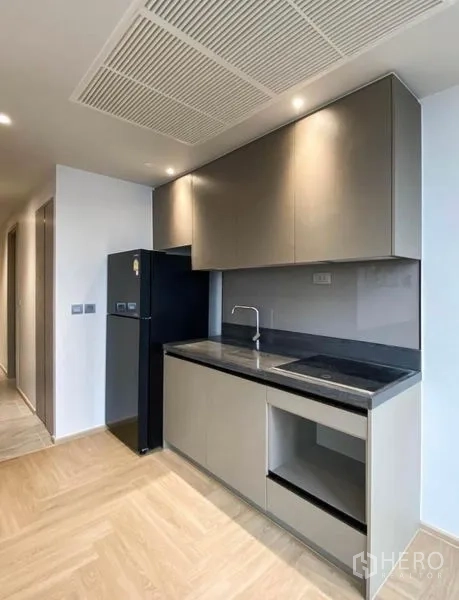 Condominium for rent in Din Daeng, Bangkok - Minimalist galley kitchen with grey cabinetry, black countertop and built-in sink.