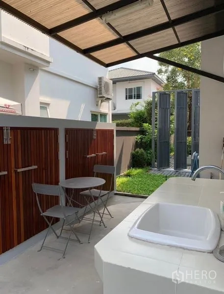Detached House for rent in Bang Phli, Samut Prakan - Covered outdoor utility area with sink, wood storage cabinets and a small bistro set.