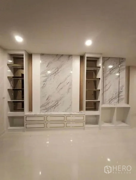 Detached House for rent or sale in Prawet, Bangkok - Feature wall with marble-look paneling, shelves and low cabinets in the living room.
