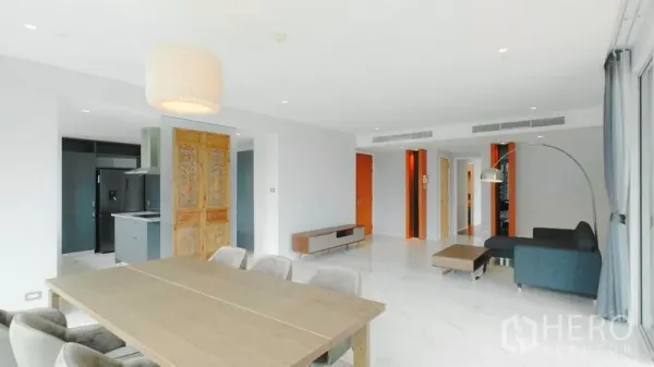 คอนโด ขาย - พื้นที่นั่งเล่นและรับประทานอาหารแบบโอเพ่น พื้นเงา โต๊ะไม้ และประตูไม้สลักในคอนโดสูง