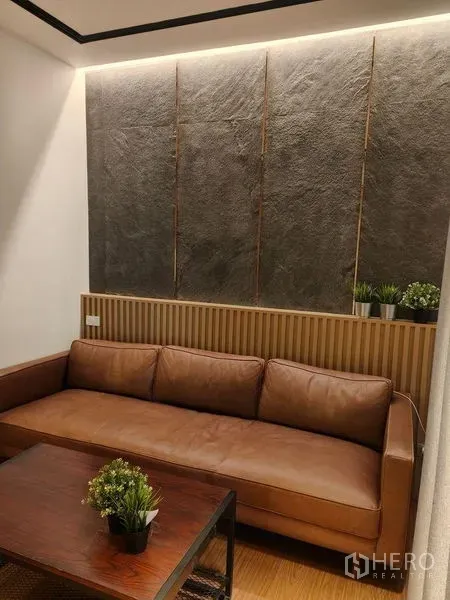 公寓 出租在Khlong Toei, Bangkok - 温馨客厅，棕色皮沙发、岩纹特色墙与木质茶几。