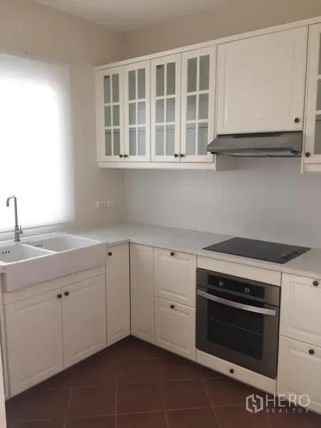 联排别墅 出租或出售在Wang Thonglang, Bangkok - 明亮的白色L形厨房，带农舍水槽、玻璃柜、炉灶和嵌入式烤箱。