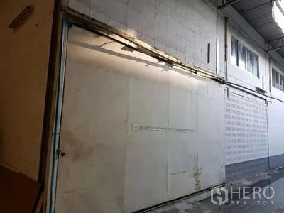 Warehouse for rent in Chatuchak, Bangkok - Close-up of a large white sliding warehouse door beneath a metal canopy with exterior lighting and concrete flooring.