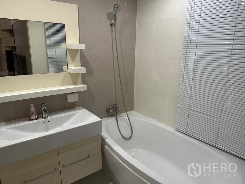 Condominium for rent in Watthana, Bangkok - Bathroom view with vanity, mirror and bathtub with handheld shower.