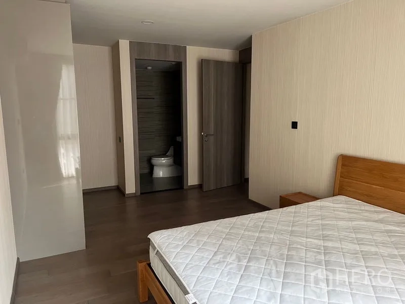 公寓 出租在Pathum Wan, Bangkok - 主卧配木床与木地板，带套内卫生间入口。