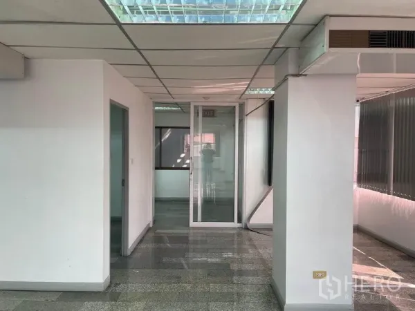 Office Space for rent in Khlong Toei, Bangkok - Entrance corridor of the office floor with a glass door, white walls and grid ceiling lighting.