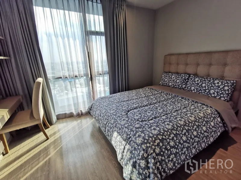 Condominium for rent or sale in Watthana, Bangkok - Second bedroom with upholstered headboard, writing desk, and floor-to-ceiling windows overlooking the city.